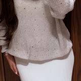 Blusa de punto blanca con mangas largas y escote en pico adornada con pedrería.
