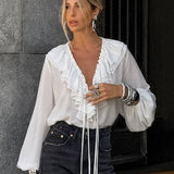 Blusa blanca con volantes, escote en pico y mangas farol.