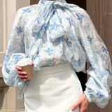 Elegante blusa con mangas farol y cuello atado, adornada con flores.