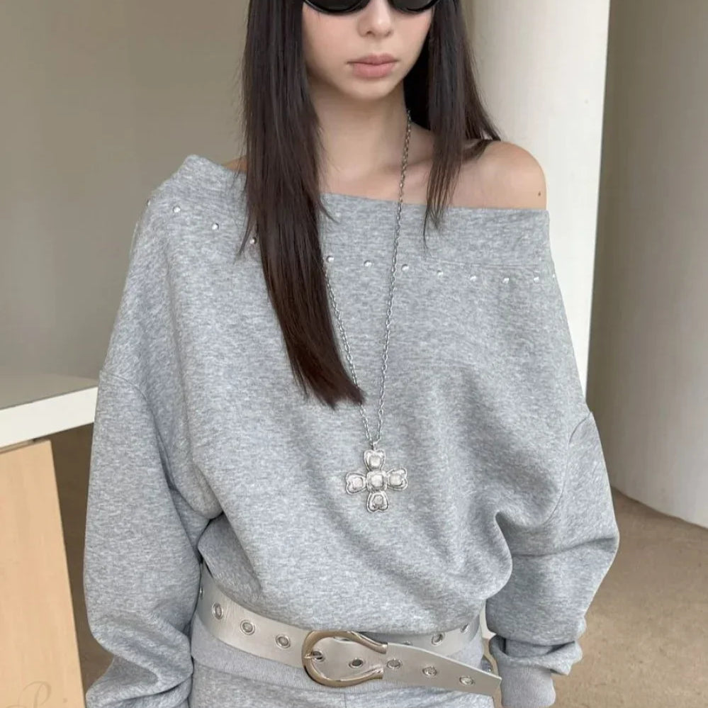 Sudadera asimétrica con hombros descubiertos, remaches y corte holgado.
