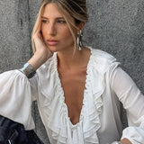 Blusa blanca con volantes, escote en pico y mangas farol.
