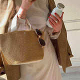 Elegante bolso de mano de paja tejida, estilo casual de playa, con asa superior y correa para el hombro.