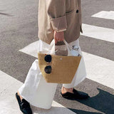 Elegante bolso de mano de paja tejida, estilo casual de playa, con asa superior y correa para el hombro.