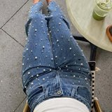Jeans con cintura asimétrica, top cruzado, detalle de perlas y piernas rectas deshilachadas.