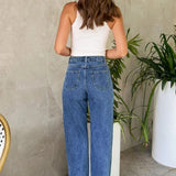 Jeans con cintura asimétrica, top cruzado, detalle de perlas y piernas rectas deshilachadas.