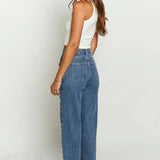 Jeans con cintura asimétrica, top cruzado, detalle de perlas y piernas rectas deshilachadas.